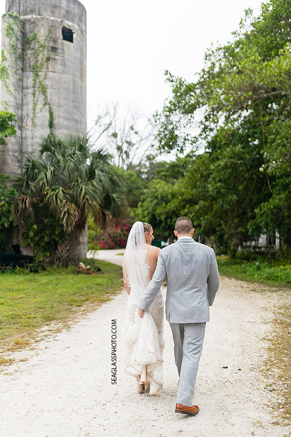 Groom carries his wife's train as they walk back to their wedding party in Vero Beach Florida