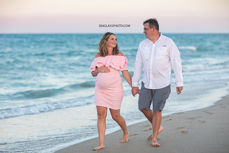 Expecting couple walking on the beach at sunset in Vero Beach Florida