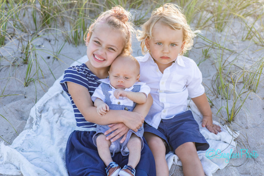 Siblings holding newborn boy on the sand in Vero Beach Florida Newborn Photographer