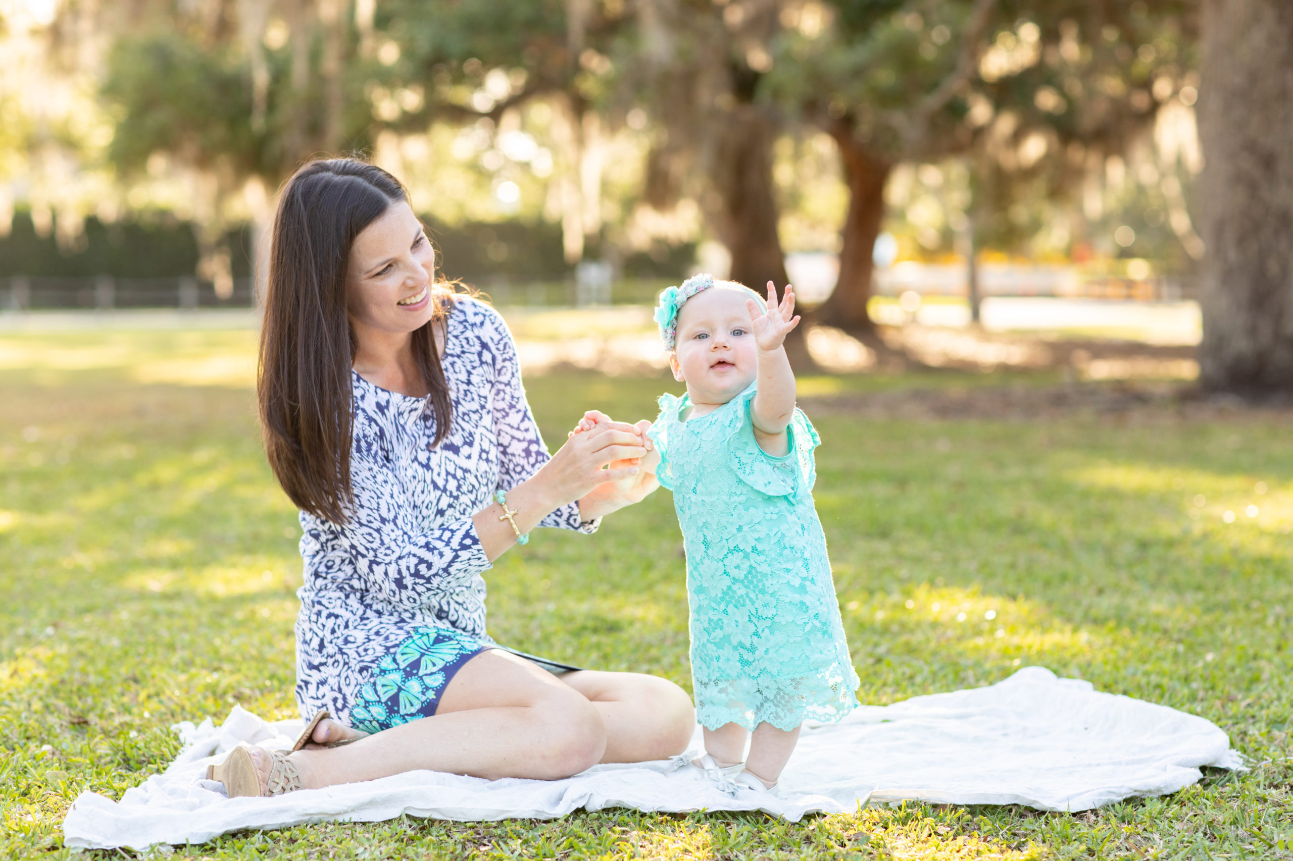Mother and daughter smiling and waving at the camera while sitting on the grass