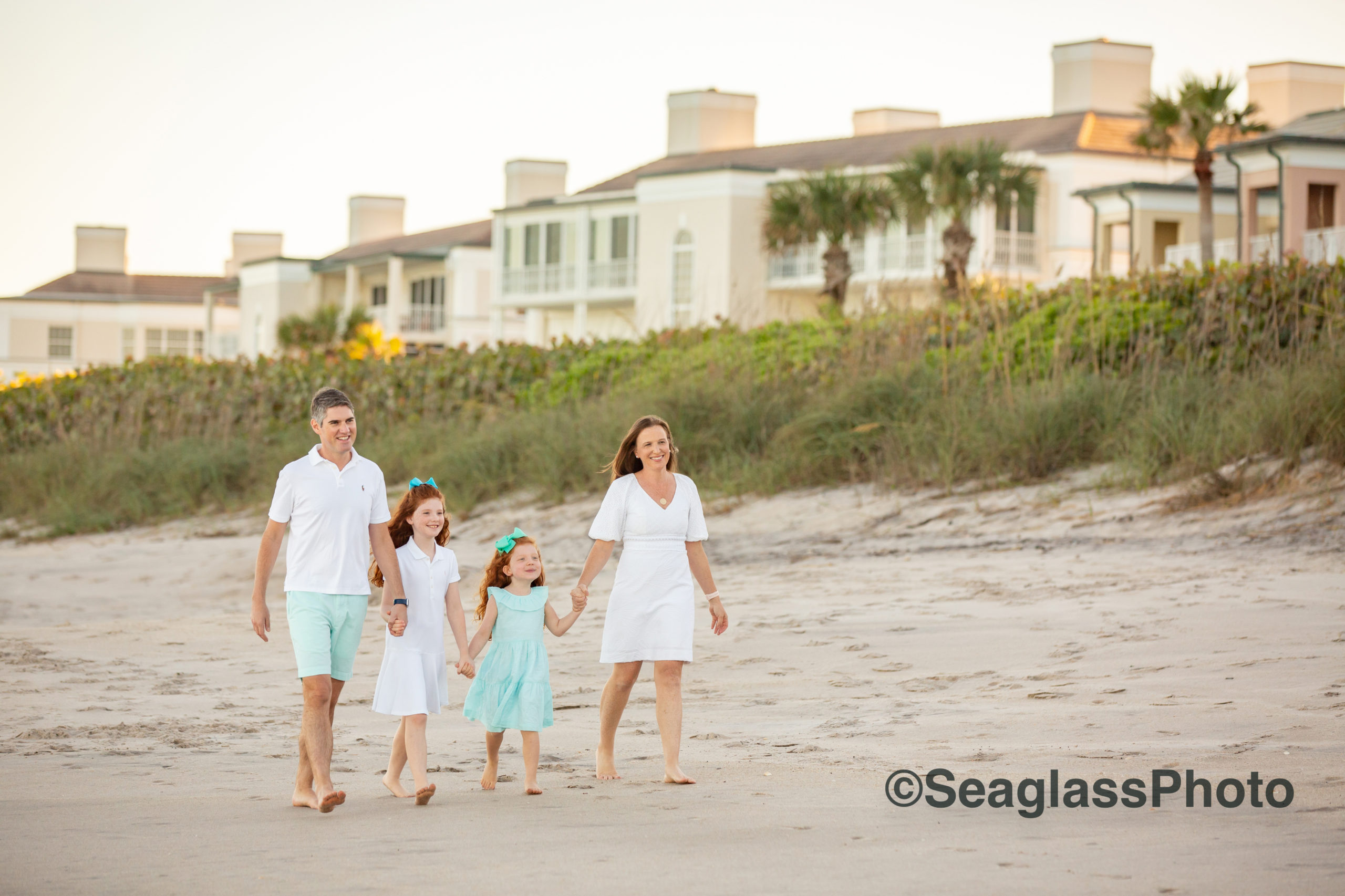 beautiful family walking on the beach in front of the John's Island Condos in Vero Beach Florida. The family is wearing white and aqua