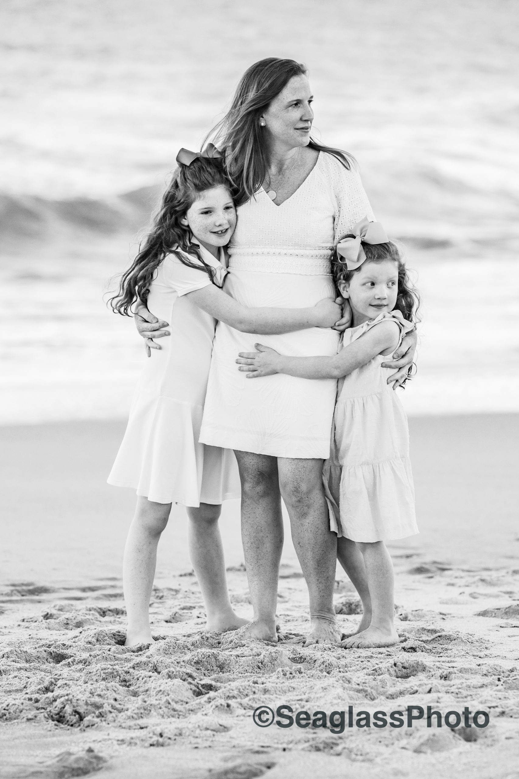 black and white photo of mom hugging daughters on the beach
