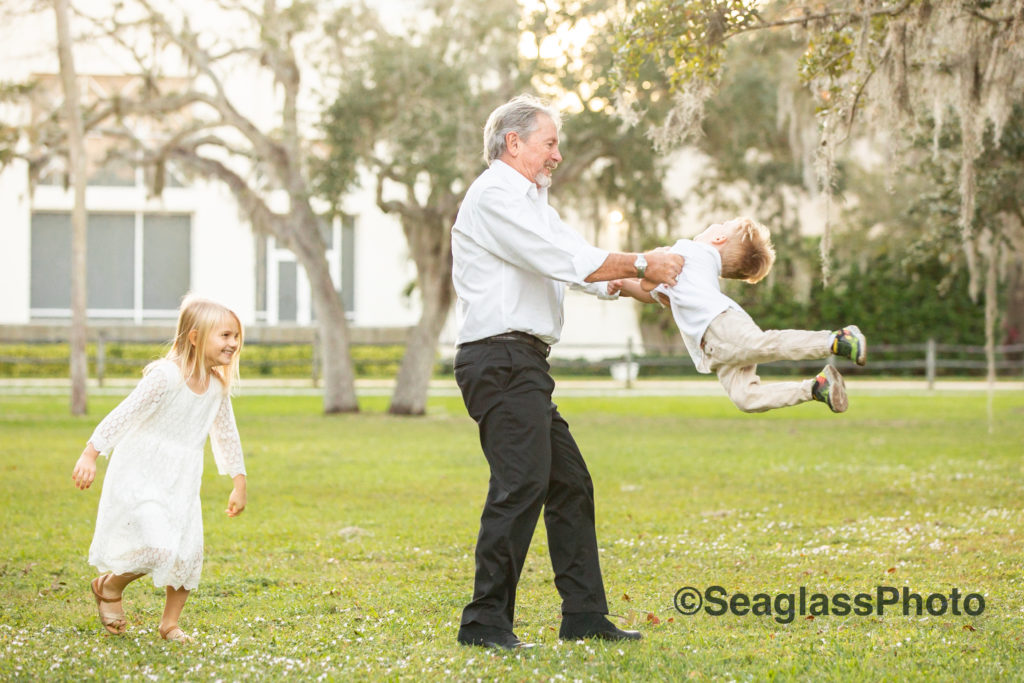 grandfather swinging grandson around surrounded by oaks at Riverside Park in Vero Beach Florida 