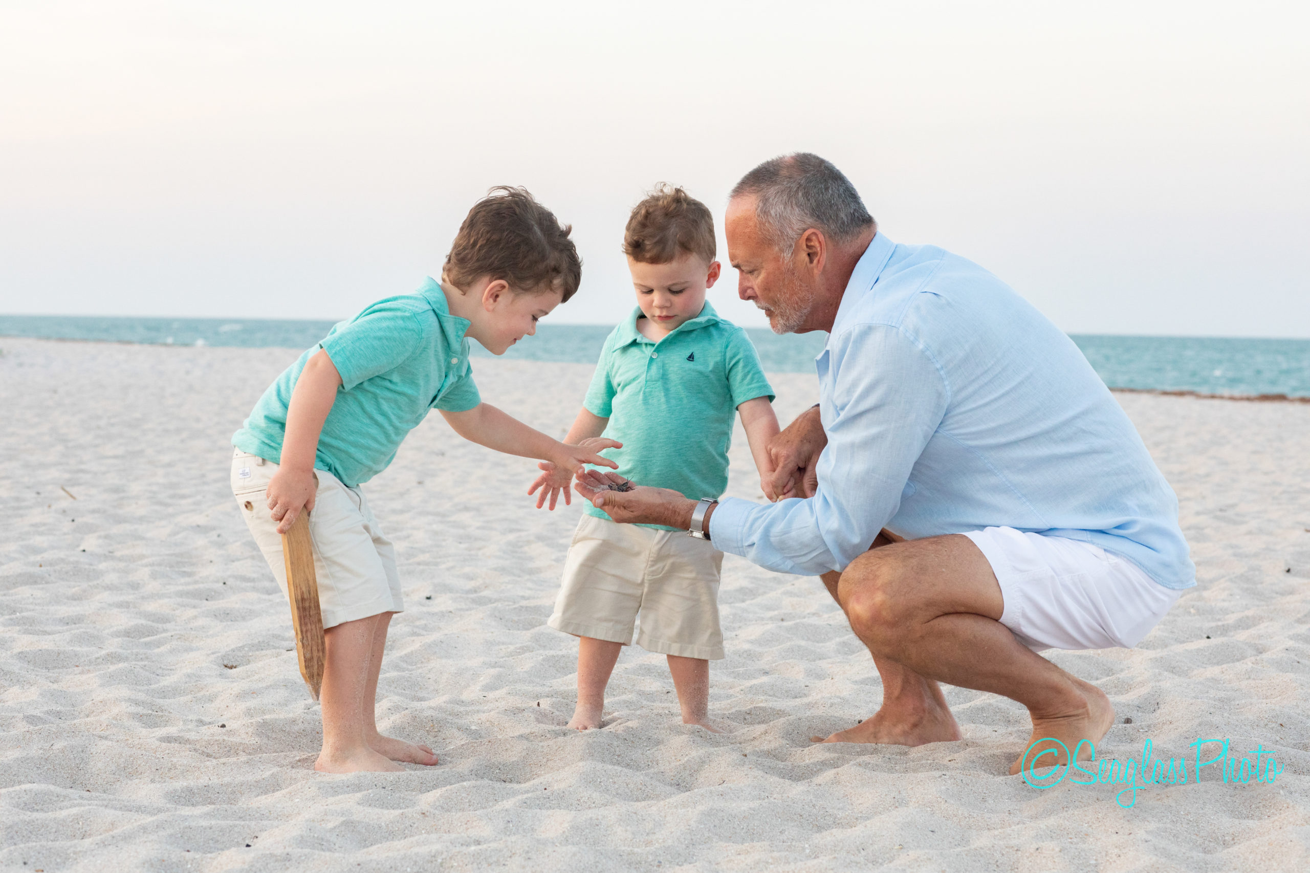 grandfather shows grandsons a grasshopper while on the beach