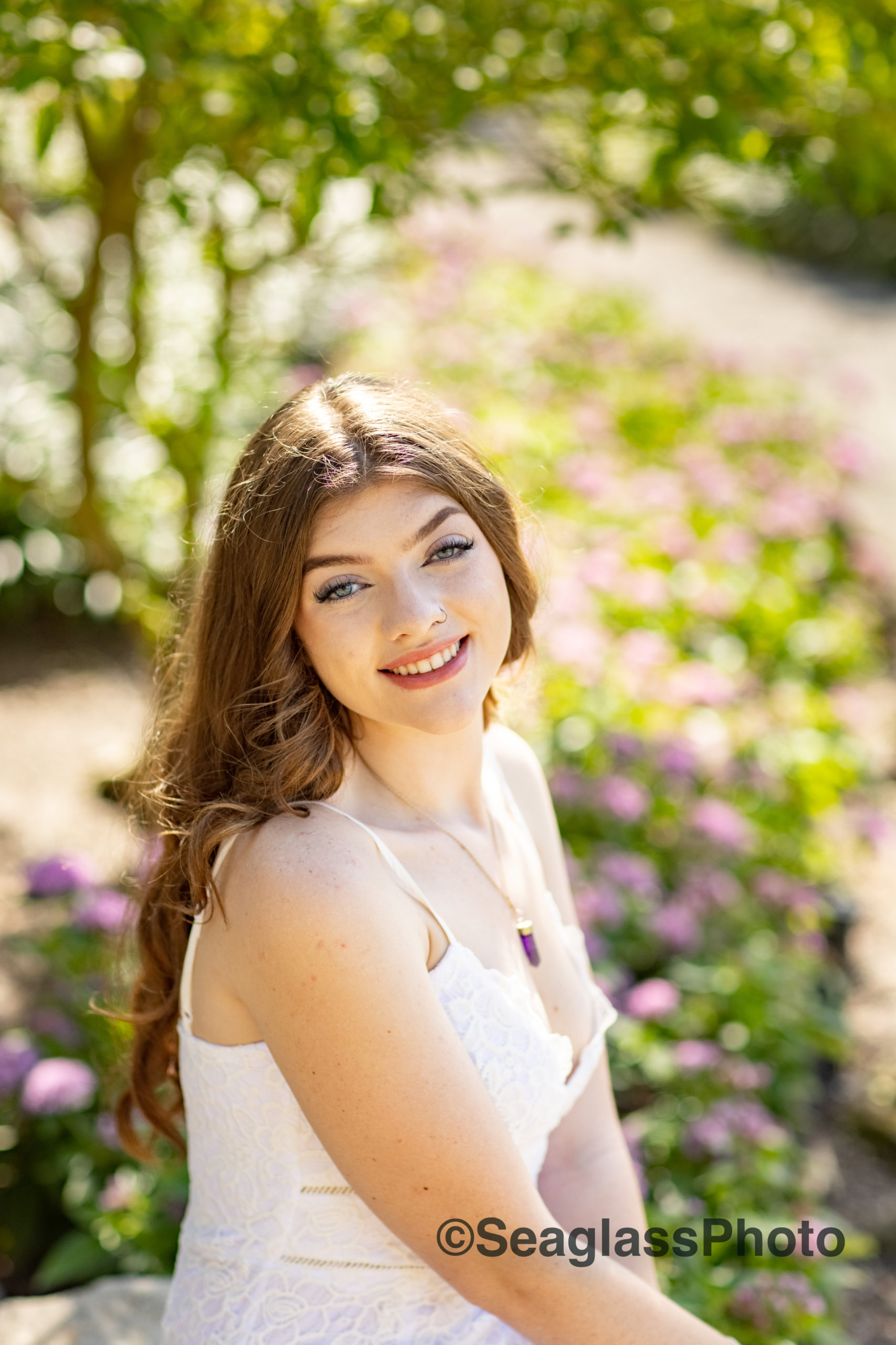 high school senior girl with long brown hair and wearing a white lace dress surrounded by purple and pink flowers at Rocky City Gardens in Vero Beach FL