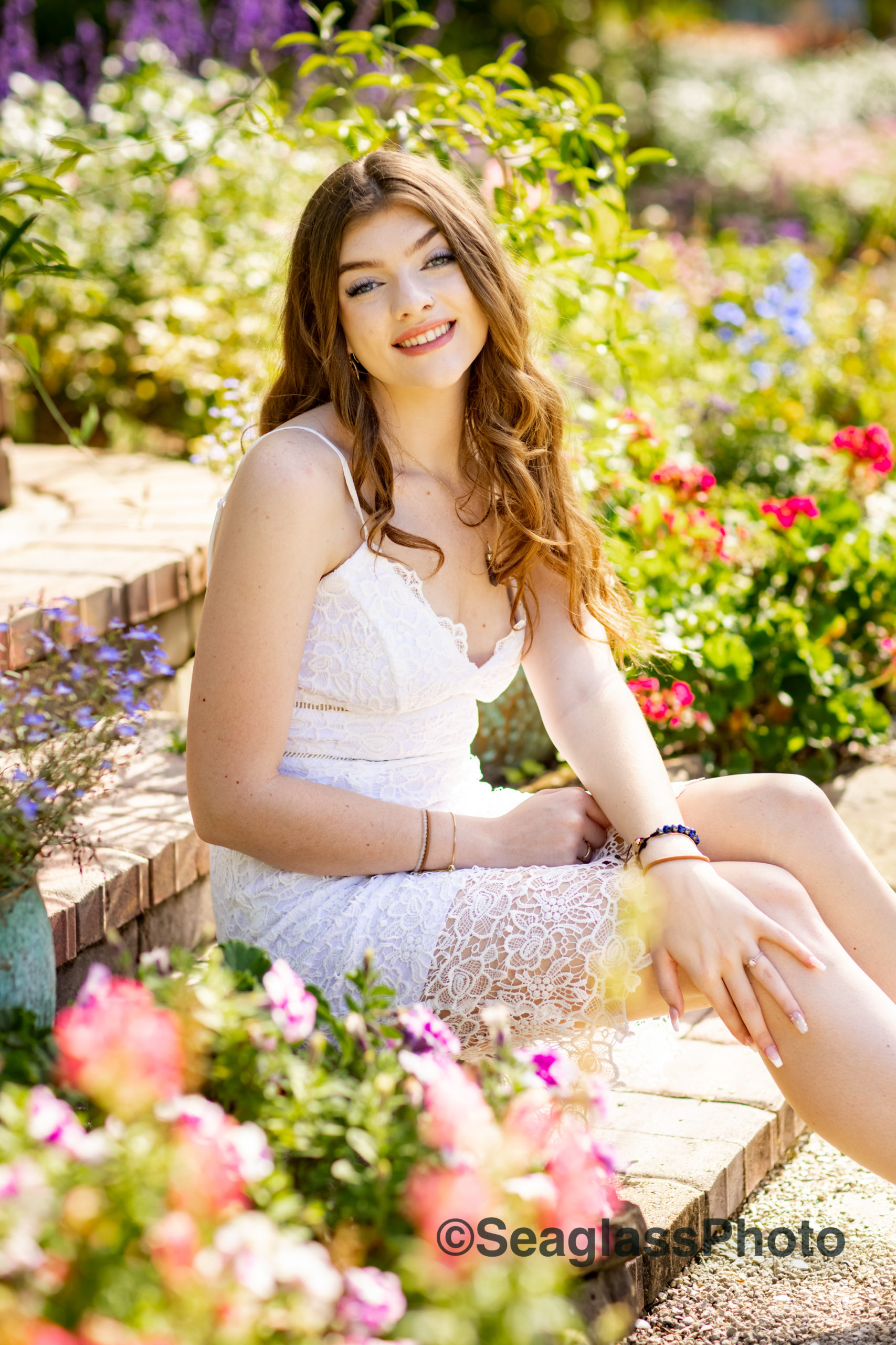 Rocky City Gardens with high school senior girl with long brown hair and wearing a white lace dress surrounded by purple and pink flowers 