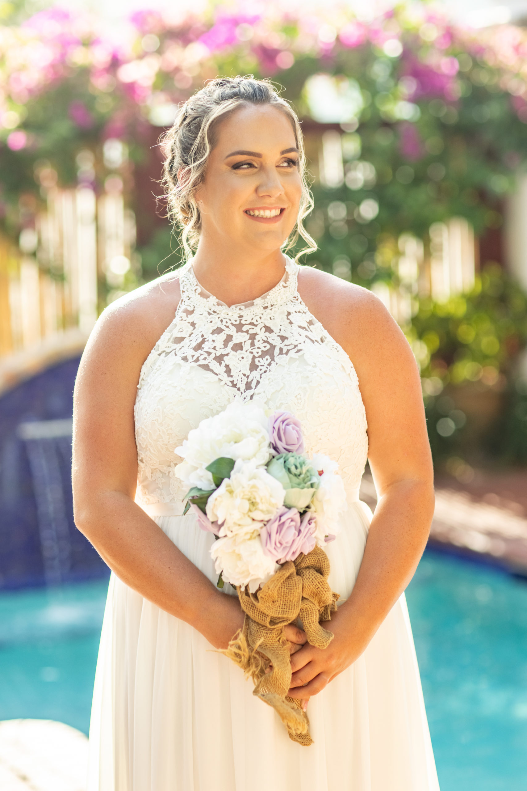 Beautiful bride standing in front of a pool and wall of flowers looking to the right 
