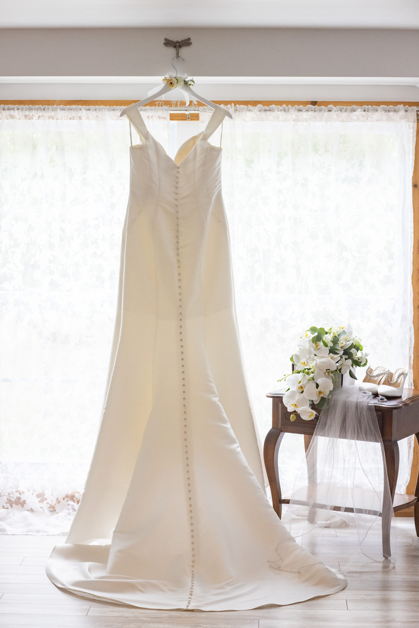 off white wedding gown with buttons down the back hanging in front of a window with lace curtains at Magnolia Manor in Vero Beach Fl 
