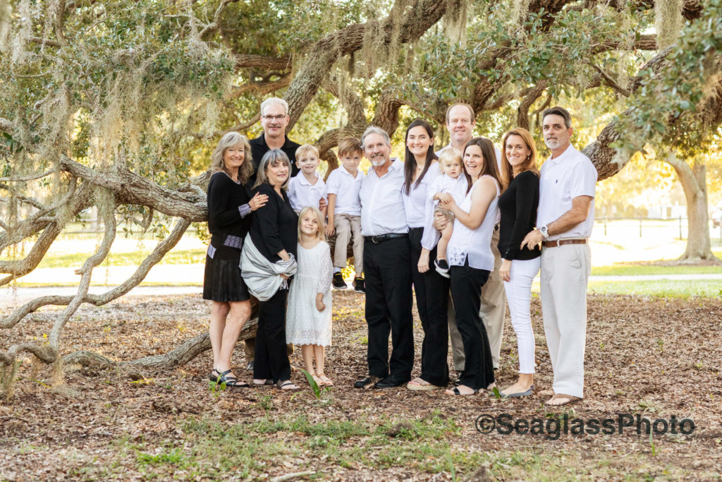 Grandparents wearing black and white standing with family under oaks of trees. 