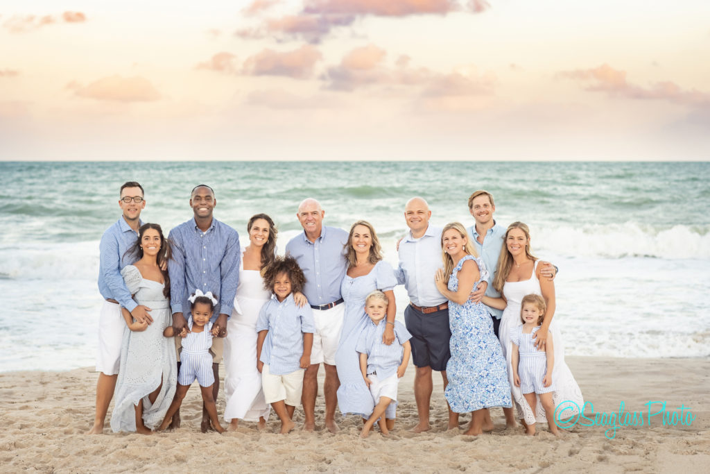 colorful sunset on the beach with a family wearing white and blue standing together for a portrait 