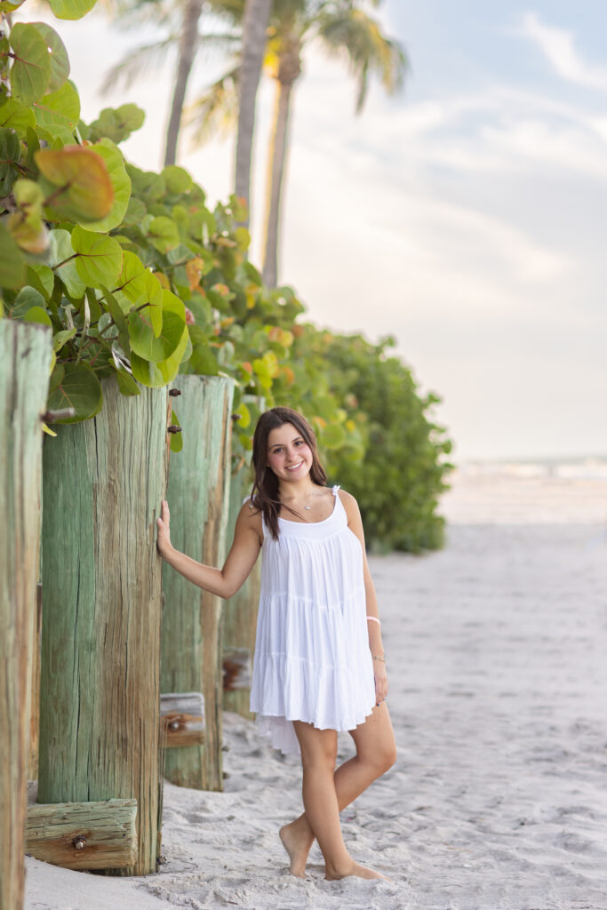 Vero Beach High School Senior Photos on the beach wearing white dress standing next to seagrapes and palm trees