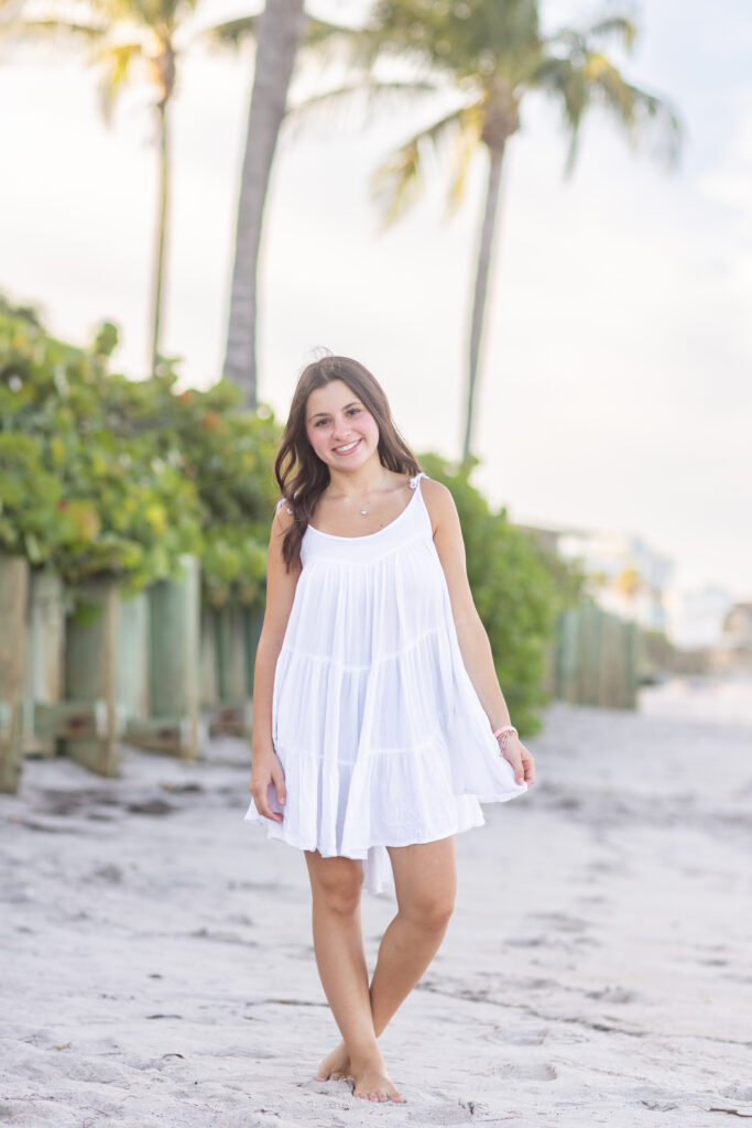 Vero Beach High School Senior Photos on the beach wearing white dress standing next to seagrapes and palm trees