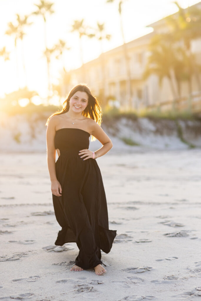 Vero Beach High School Senior Portrait wearing black dress on the sand with palm trees in the background. The sun is shining and beautiful 