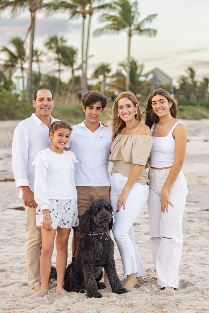 beautiful sunset portrait of a family wearing white and khaki and a black goldendoodle and palm trees in the background at Moorings in Vero Beach