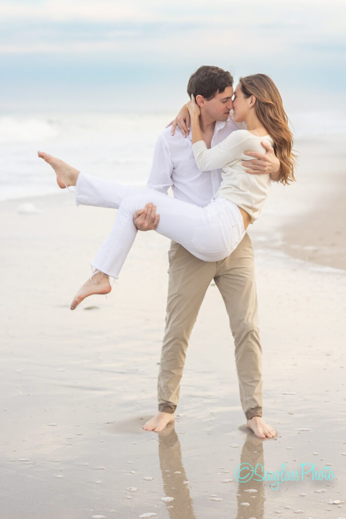 man holding his fiance in an embrace going in for a kiss while standing on the sand at John's Island Beach Club in Florida