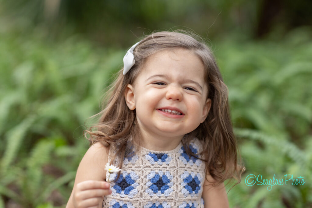 portrait of a toddler girl wearing a beige and blue dress and holding a daisy flower on Sandfly Lane in Vero Beach