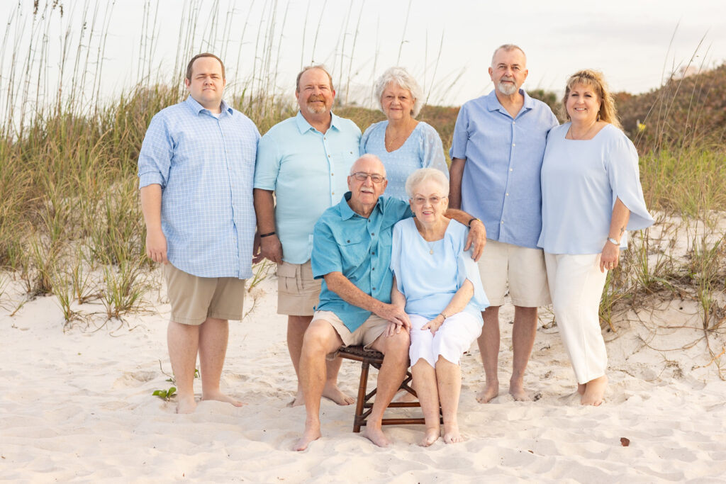 family wearing blue, khaki, and teal on the beach in front of dunes with wispy green grass