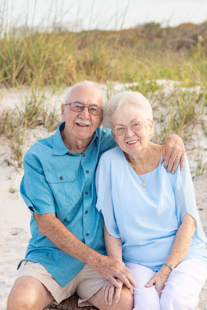 beautiful portrait of grandparents sitting on a wooden bench at the beach with dunes in the background