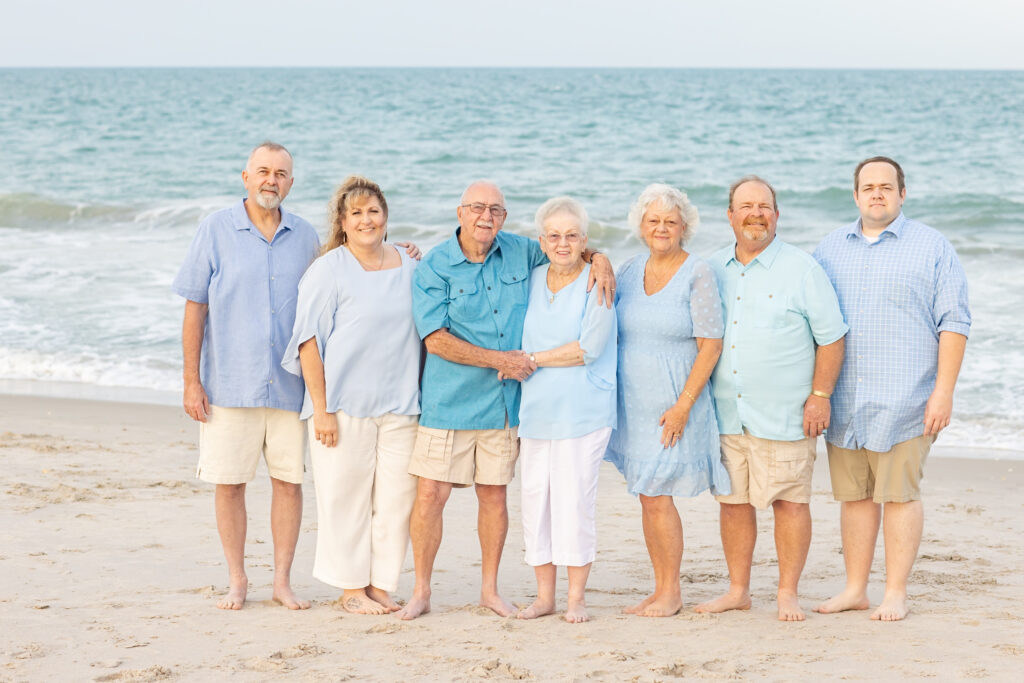 adult families wearing white, blue, khaki and teal standing on the beach for a family photo in Vero Beach Florida 