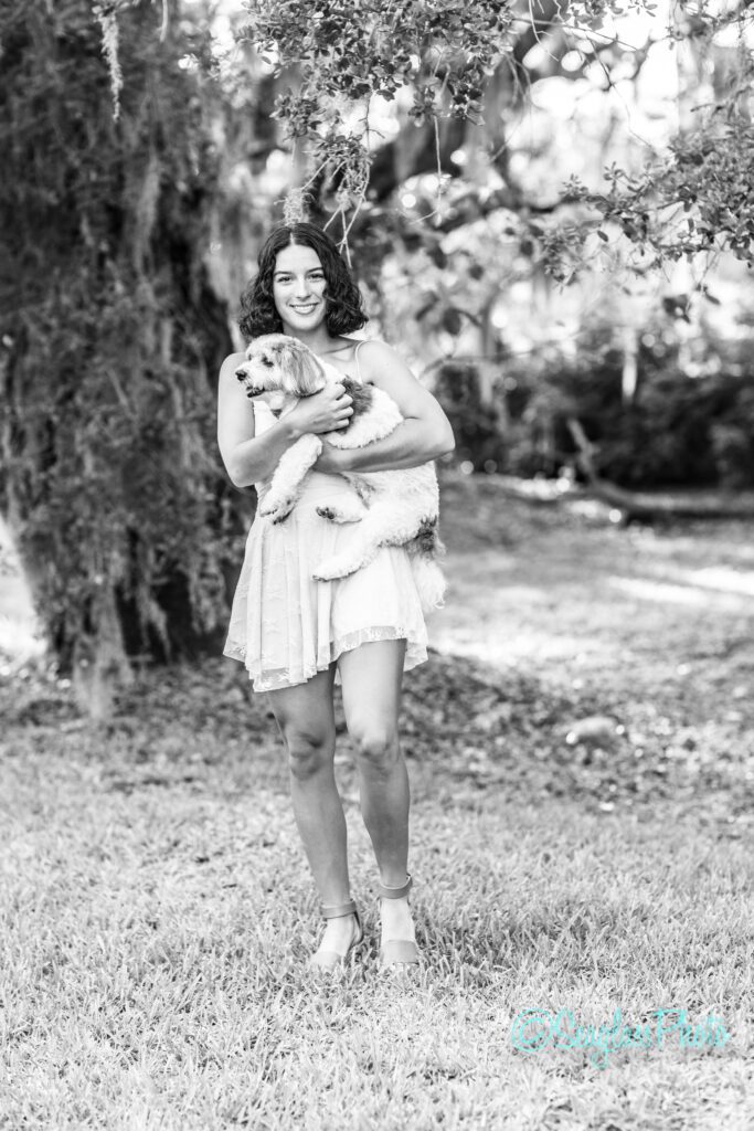 Black and white portrait of a high school senior girl holding her dog under oak trees
