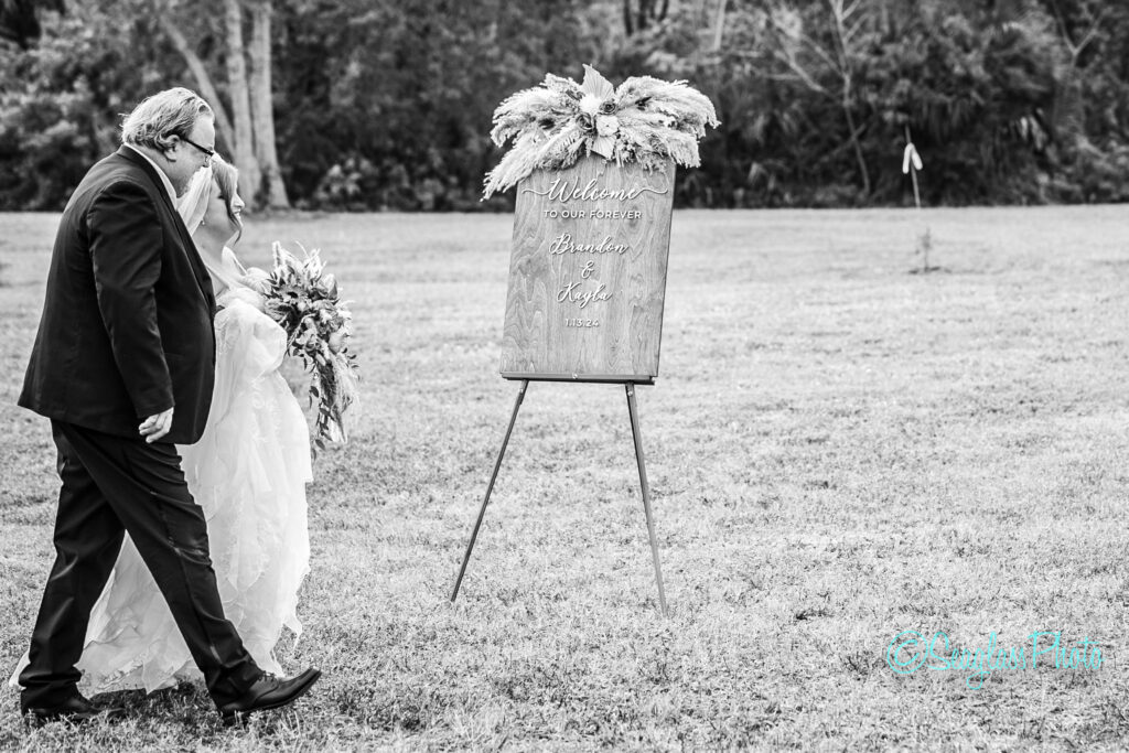 Black and white photo of a dad walking his daughter to a backyard wedding ceremony