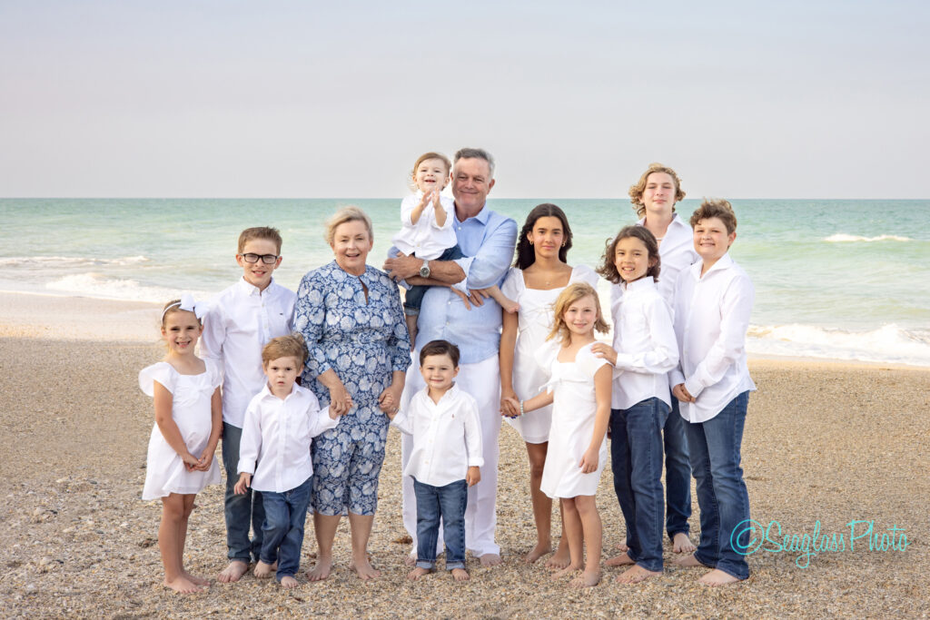 grandparents wearing blue standing on a beautiful beach at sunset with their grandkids wearing white and jeans in Vero Beach Florida 