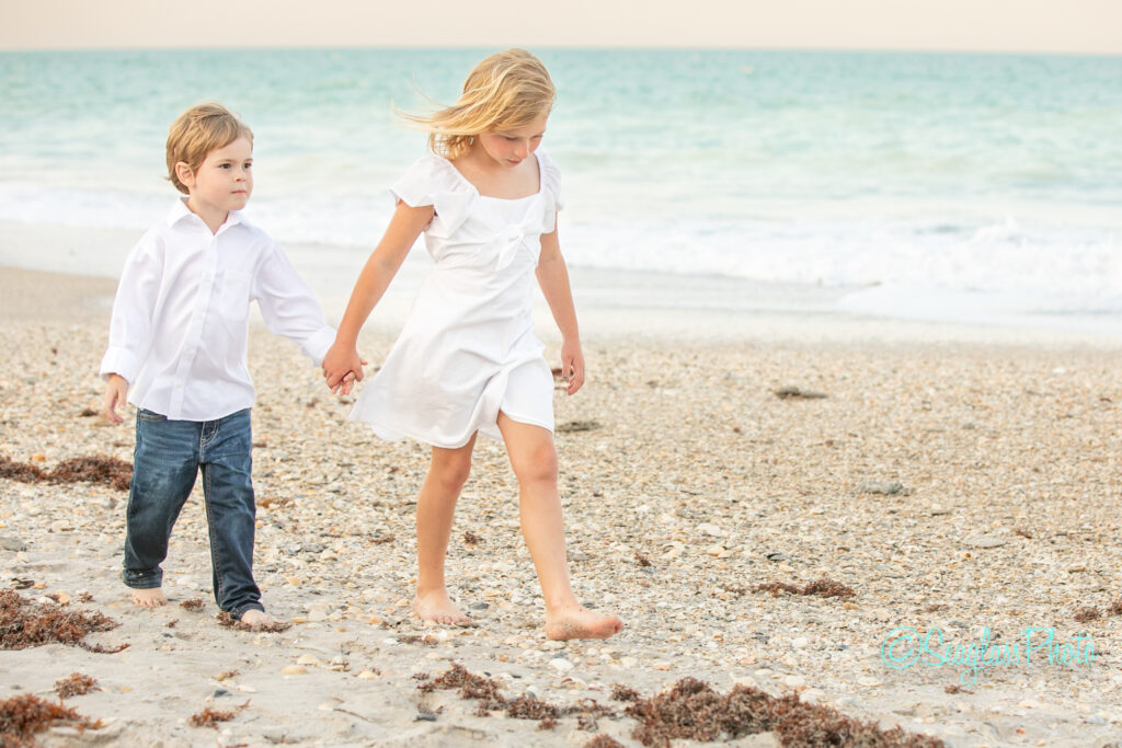 Older sister walking and holding hands with her younger brother at sunset on the beach in Florida 