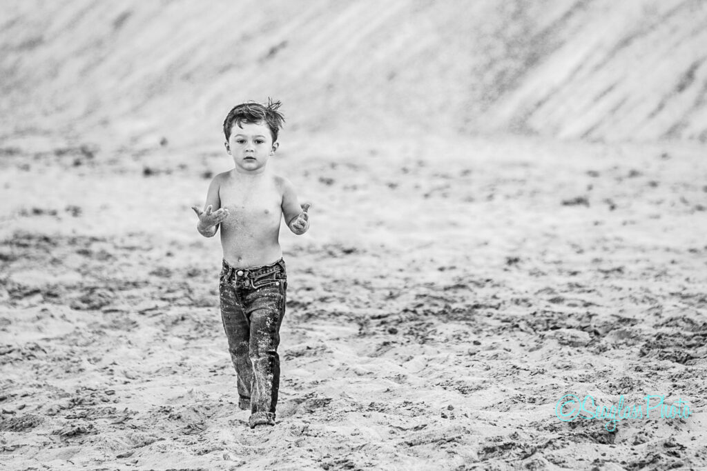 black and white photo of toddler wearing jeans covered in sand