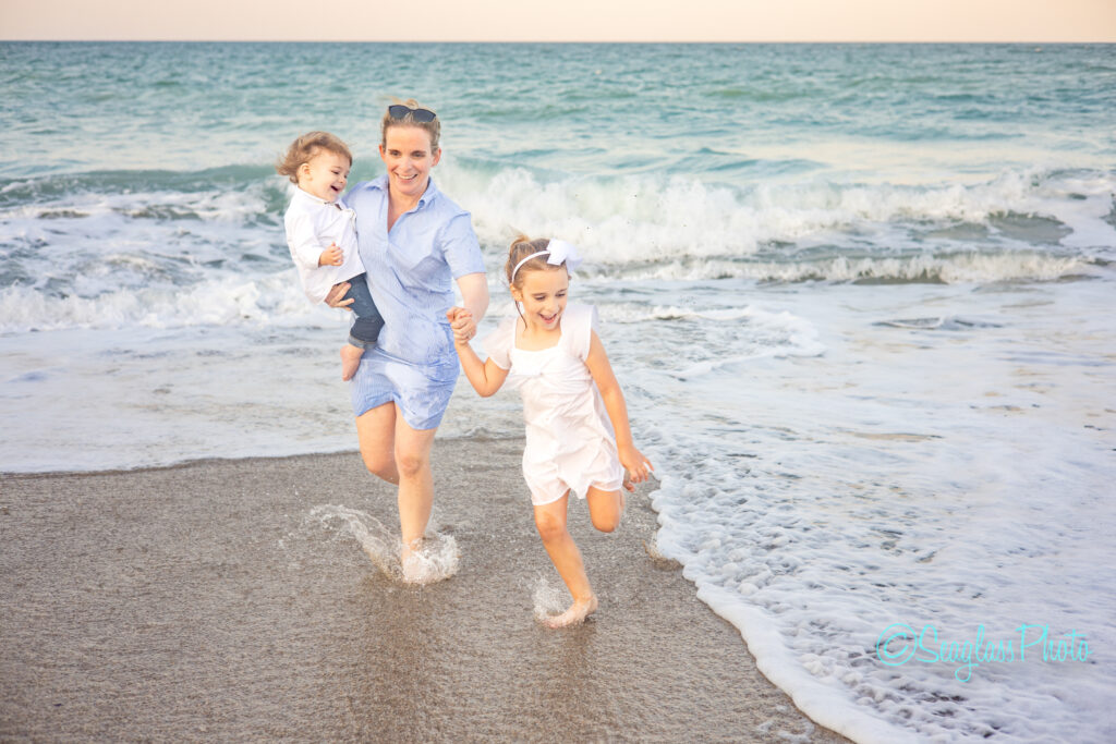 mother holding her toddler son and holding her daughters hand as the run out of the ocean at sunset in Vero Beach Florida 