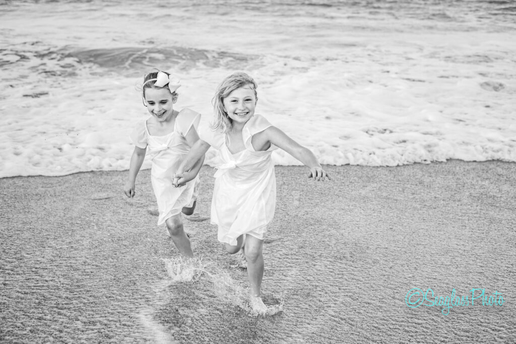 black and white photo of sisters wearing white dresses running out of the ocean