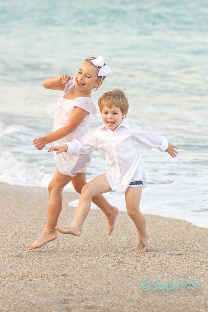 siblings wearing white running around in the waves at the beach in Vero Beach Florida 