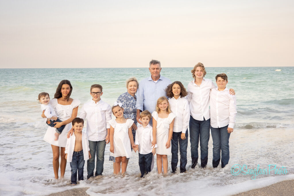 grandparents wearing blue standing on a beautiful beach at sunset with their grandkids wearing white and jeans in Vero Beach Florida 