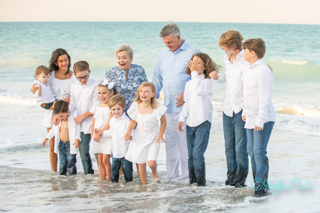 grandparents wearing blue standing on a beautiful beach at sunset with their grandkids wearing white and jeans in Vero Beach Florida 