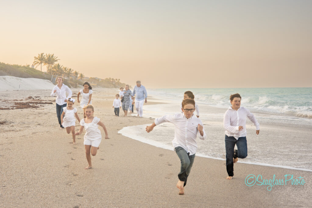 grandparents wearing blue running on a beautiful beach at sunset with their grandkids wearing white and jeans in Vero Beach Florida 