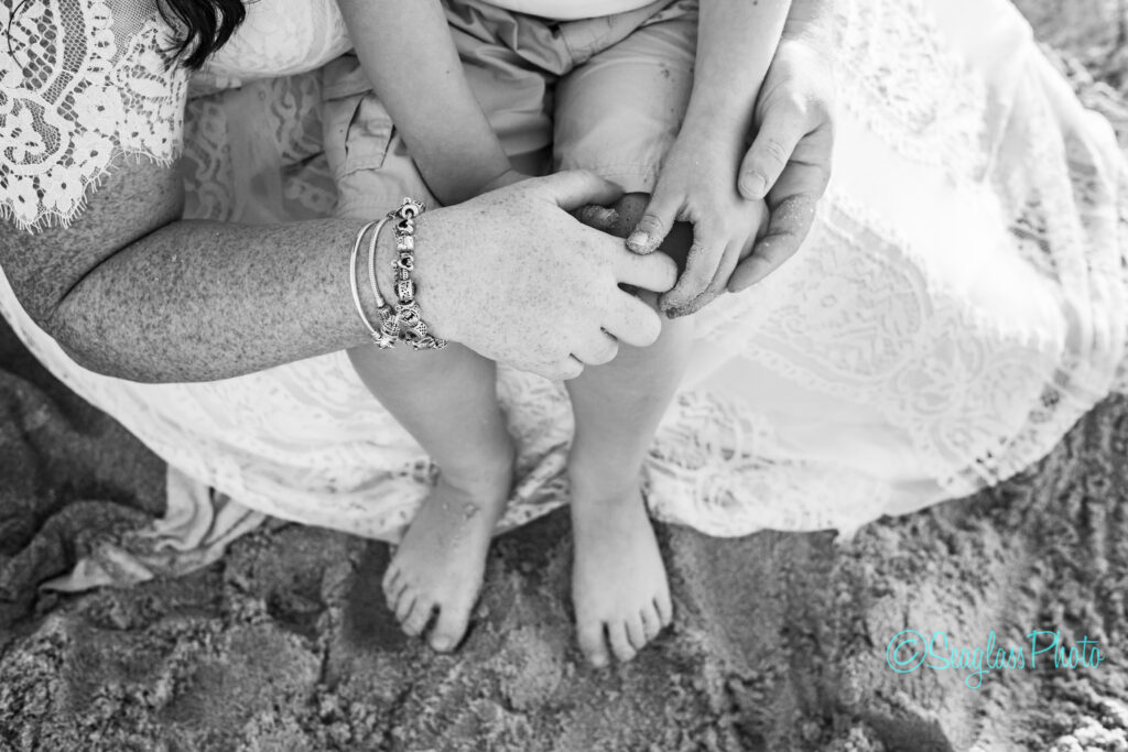 black and white photo of mother holding sons hands while sitting on the sand 