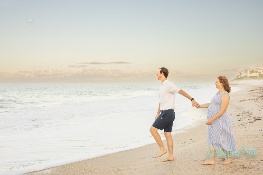 pregnant woman and husband holding hands by the ocean at the Vero Beach Disney resort photoshoot