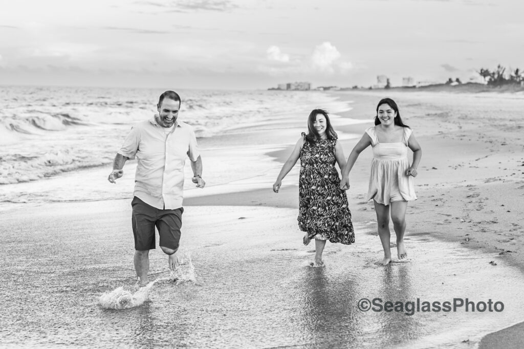 Black and white photo of family running on the beach with the water splashing up 