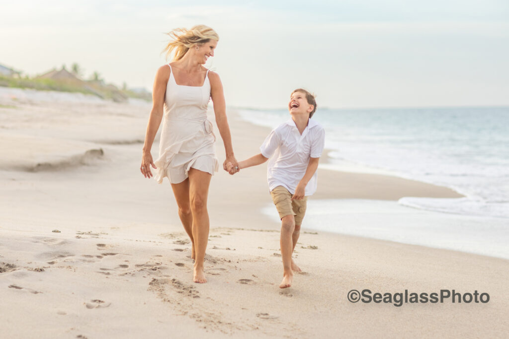 mother and son skipping down the beach family portrait in Vero Beach Florida wearing a mix of white, khaki and cream