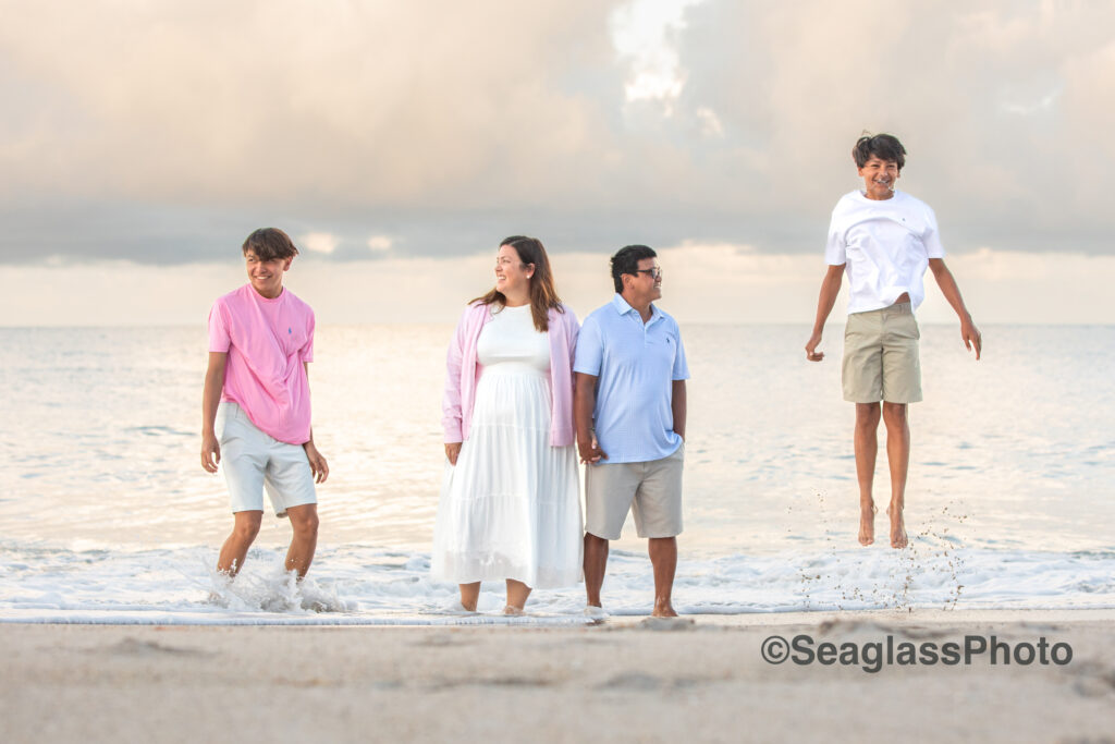 unique disney family beach photoshoot of parents holding hands watching their teen sons jumping out of the water 