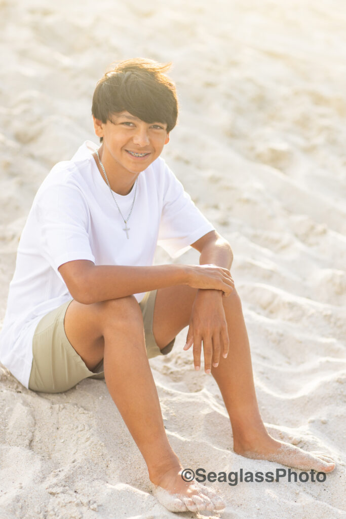 teen boy sitting on the beach wearing a white shirt and khaki shorts with a silver cross necklace at the Disney Vero Beach Resort