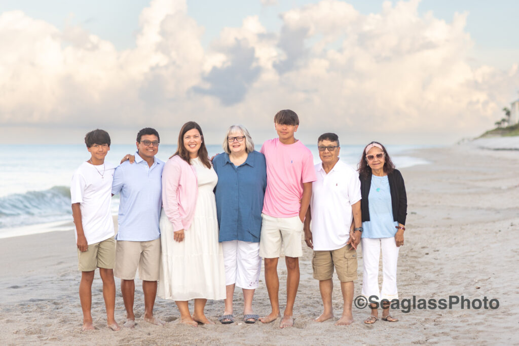 family portrait on the beach at sunset in front of Disney Vero Beach Resort. The family is wearing pink, white and blue