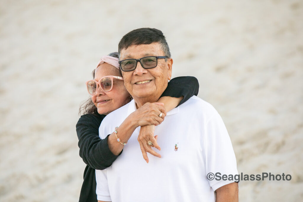 wife hugging onto her husband on the beach at the Disney Vero Beach Resort wearing sunglasses 