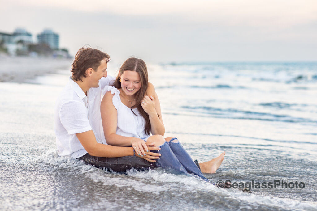 couple wearing white shirts and jeans sitting on the  beach in Vero Beach Florida engagement photoshoot