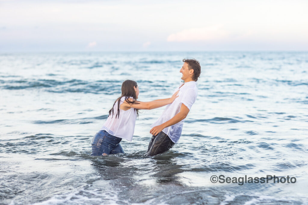 couple wearing white shirts and jeans standing in the ocean in Vero Beach Florida engagement photoshoot