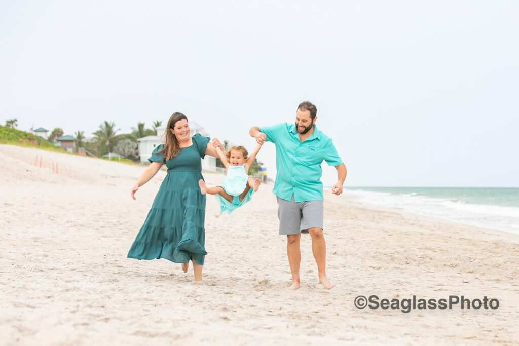 mom and dad swinging their daughter on the beach at Disney 