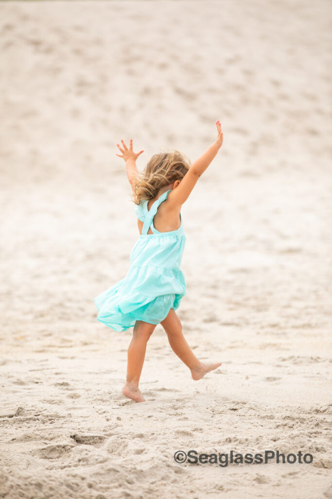 toddler girl wearing a teal dress dancing on the sand at the Vero Beach Disney Resort 