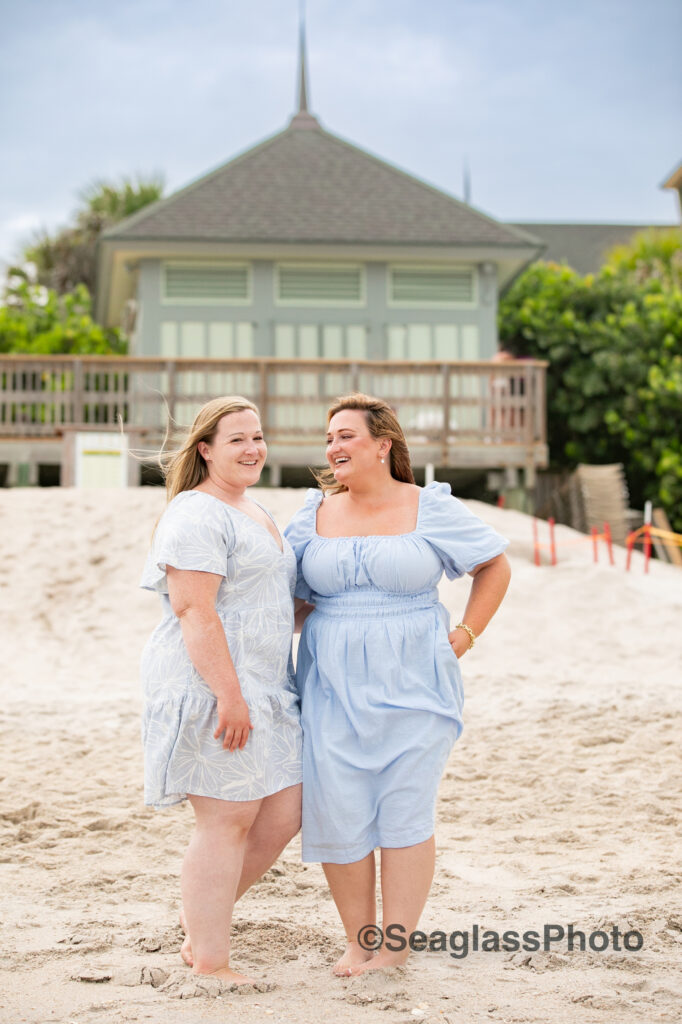 Sisters wearing blue dresses standing on the beach laughing in front of the Disney Vero Beach Resort