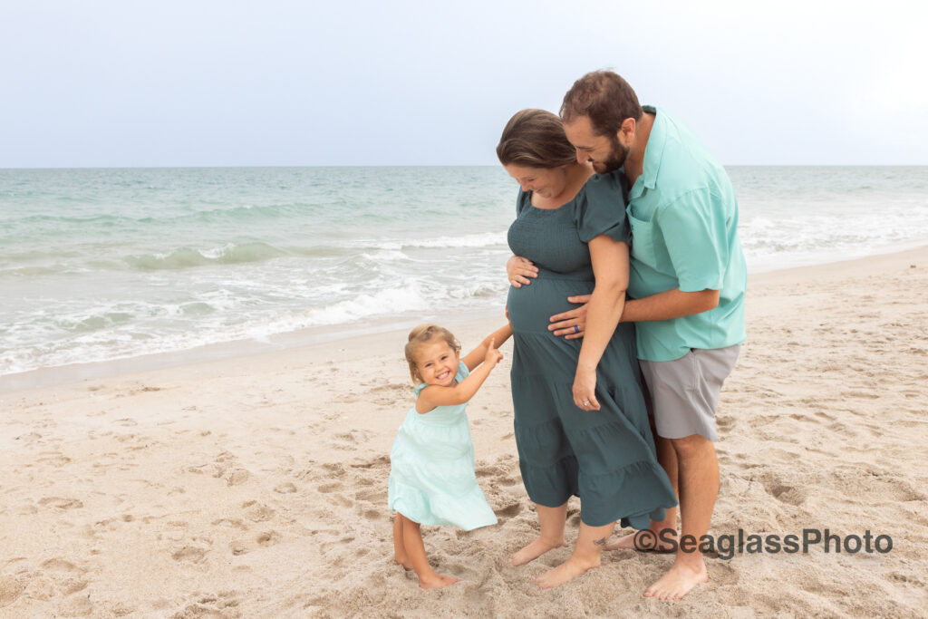 Sweet photo of a toddler girl pointing to her pregnant mom's belly on the beach at Disney Vero Beach Resort