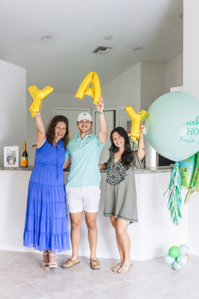 Realtor Lori Strazzula of Compass is standing next to a couple in their first home buy and holding balloons that spell YAY