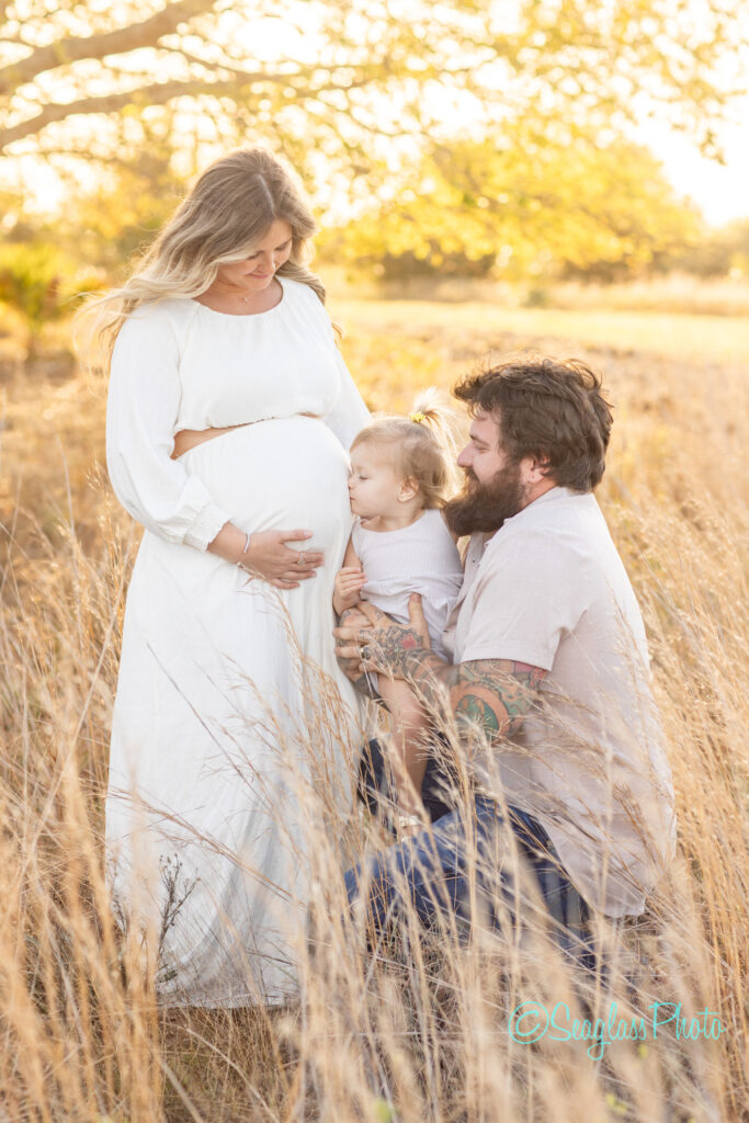 a pregnant woman wearing a cream gown standing in the field with her family in Vero Beach photoshoot